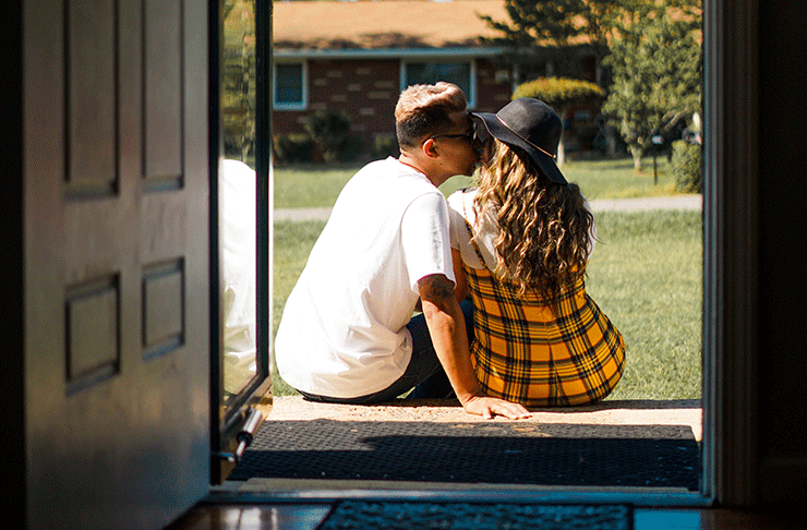 A couple sitting on their front stairs kissing.